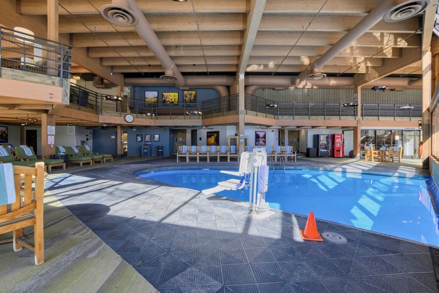A multi-level indoor pool area with lounge chairs, a diving board, and a mezzanine level with seating.