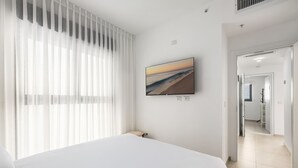 Een hotelkamer met een bed, een aan de muur bevestigde televisie en uitzicht op het strand.