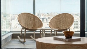 Een balkon met twee rieten stoelen en een kleine tafel met een boek en een schaal.