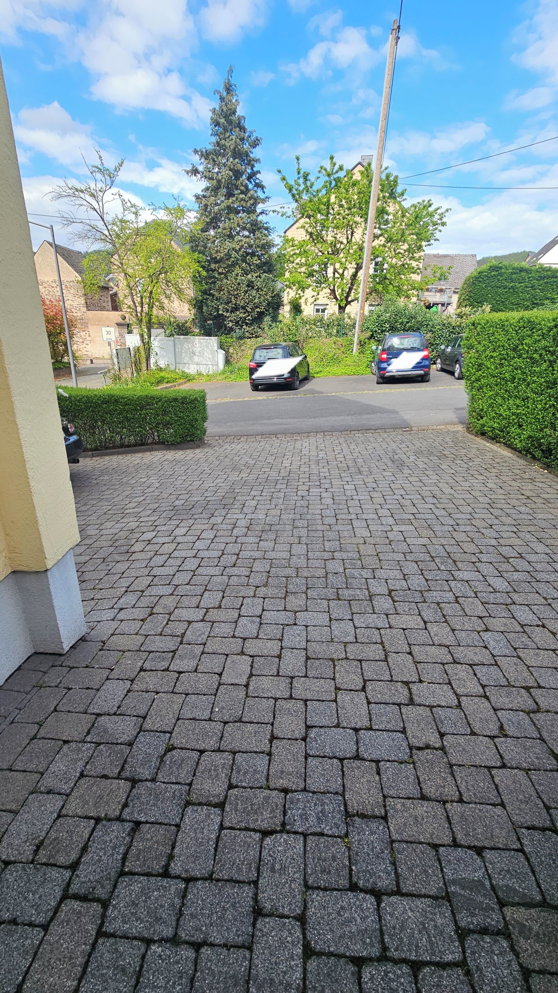 Une allée pavée menant à des voitures garées, entourée de verdure et d’immeubles résidentiels.