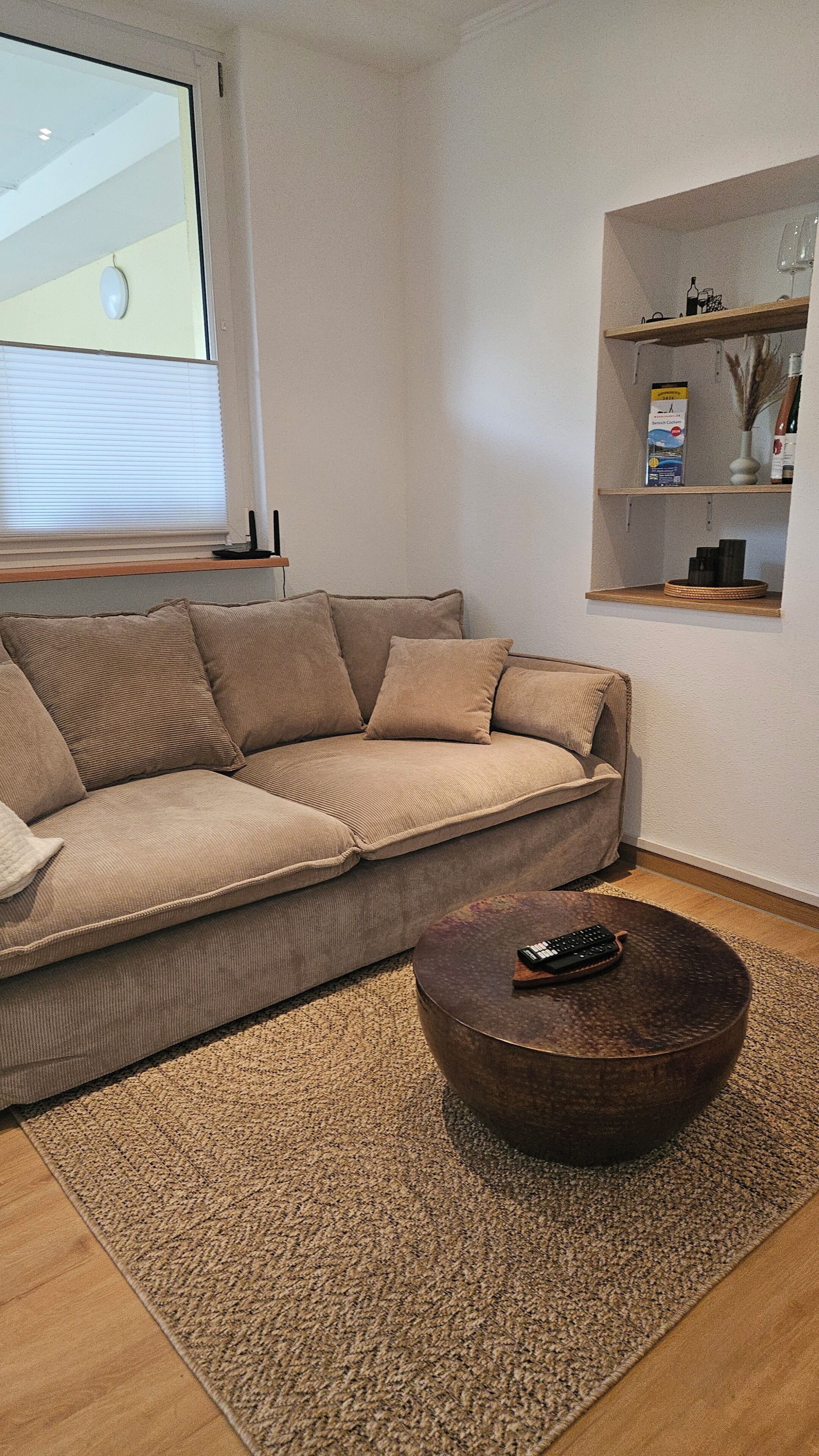 A living room with a beige sofa, a round coffee table, a rug, and a shelf with decorative items.