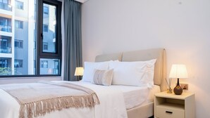 Et hotelværelse med en seng, sengeborde, en lampe og et vindue med gardiner.