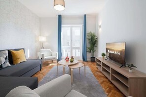 Ein modernes Wohnzimmer mit einer Couch, einem Couchtisch, einem Fernseher und einem großen Fenster mit Vorhängen.