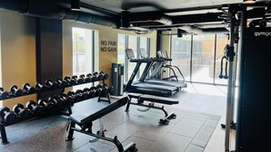 Un gimnasio con mancuernas, una banca, una cinta de correr y un letrero en la pared que dice 'NO PAIN NO GAIN'.