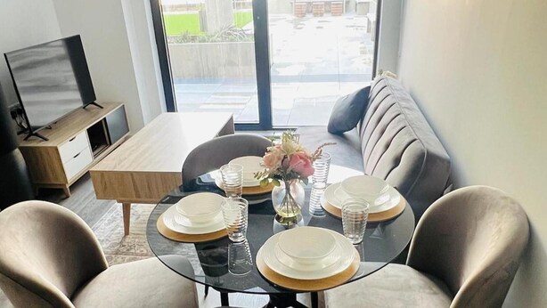 A dining area with a glass table, chairs, and a sofa. - Sleeps 3 - Garden and Parking - Near Old Trafford (Salford)