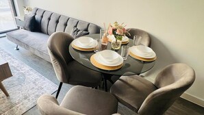 Un comedor con una mesa redonda dispuesta para cuatro personas, rodeada por cuatro sillas, un sofá y un florero con flores.