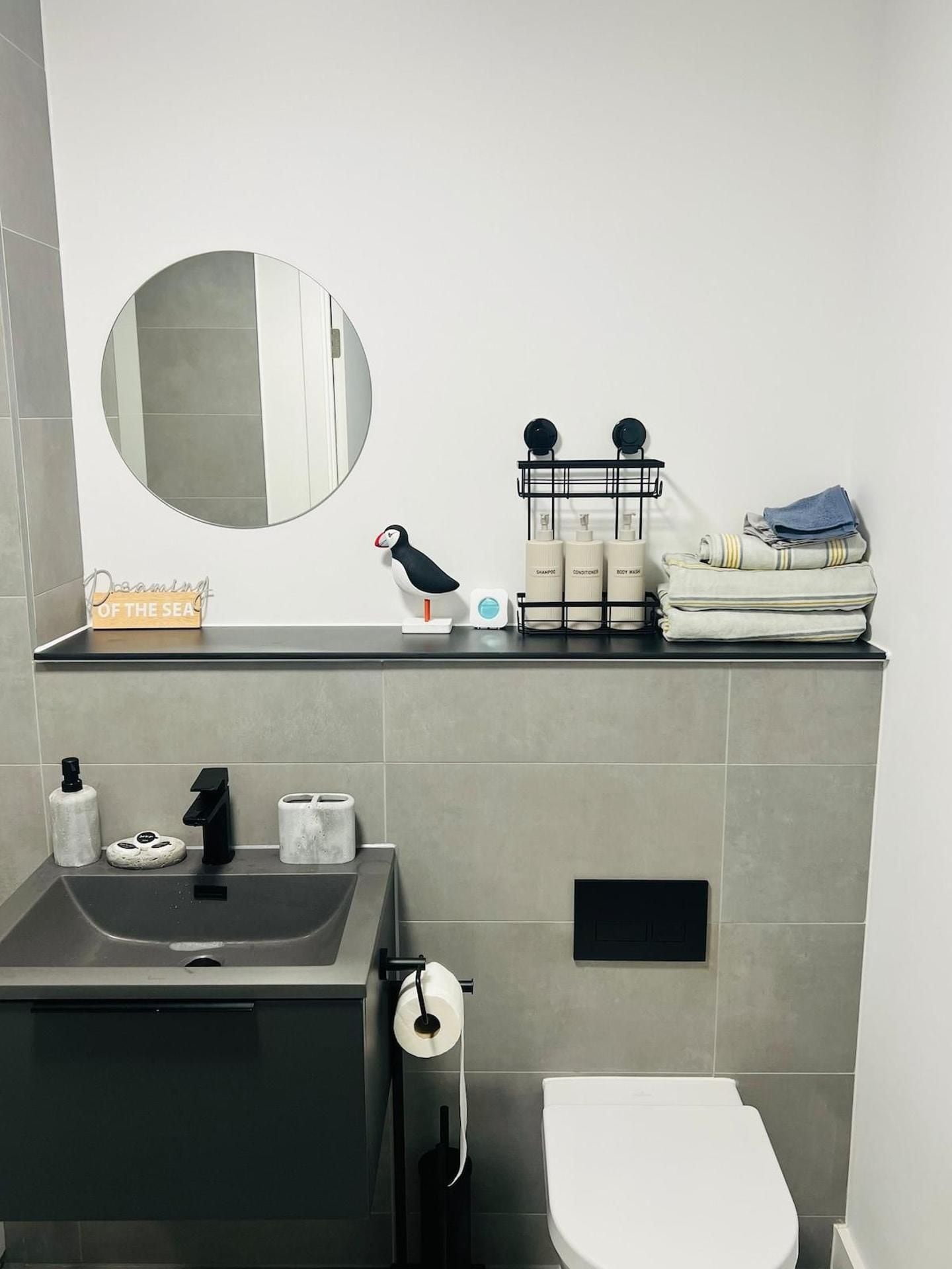 A modern bathroom with a sink, mirror, toilet, and a towel rack with folded towels.
