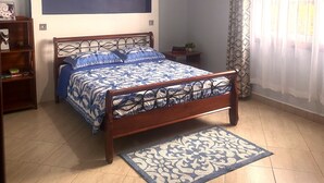 Ein Schlafzimmer mit einem Bett, einem Nachttisch, einem Bücherregal, einer Deckenleuchte und einem Fenster mit Vorhängen.