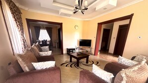 Ein Wohnzimmer mit Sofas, einem Couchtisch, einem Fernseher und einem Essbereich im Hintergrund.