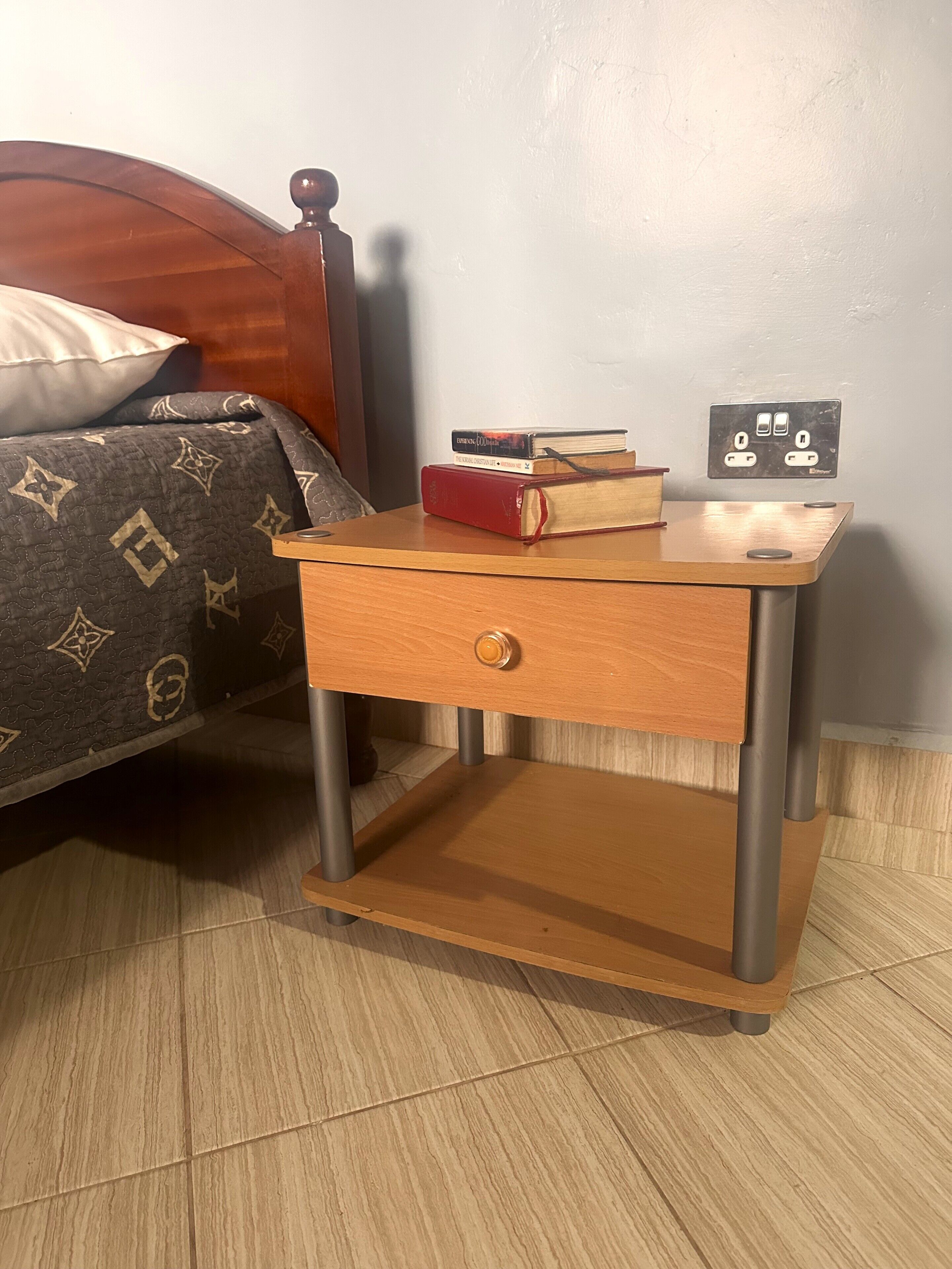 A wooden bedside table with a drawer, a small shelf, and a power outlet.