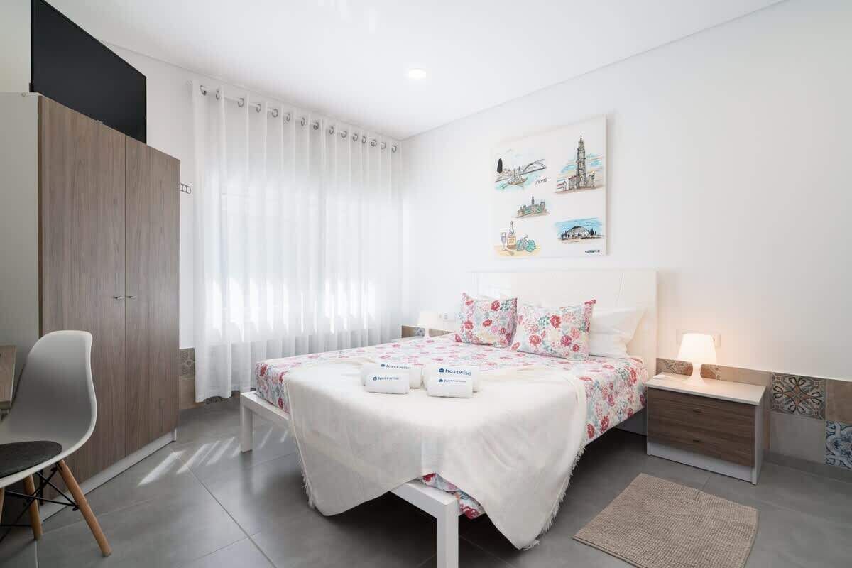 Quarto moderno com cama, cadeira, mesa de cabeceira e uma parede decorada com obras de arte.