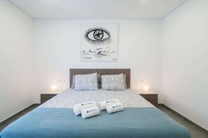 Una camera d'hotel con un letto, due comodini con lampade, un quadro appeso e asciugamani con il logo dell'hotel.