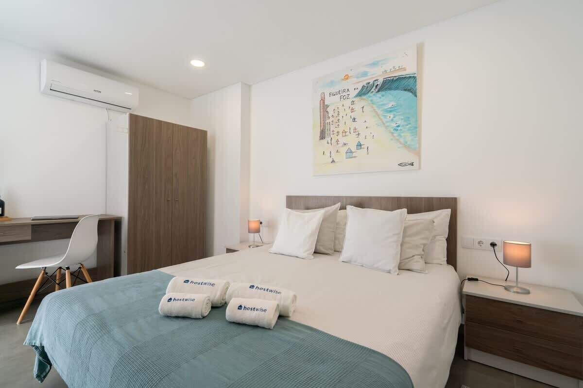 Ein Hotelzimmer mit einem Bett, einem Schreibtisch, einem Sessel, einem Nachttisch und einer Wandklimaanlage.