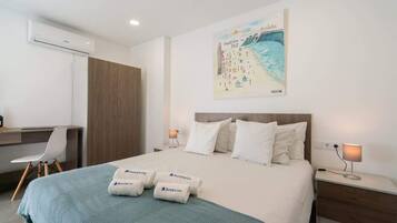 Ein Hotelzimmer mit einem Bett, einem Schreibtisch, einem Sessel, einem Nachttisch und einer Wandklimaanlage.