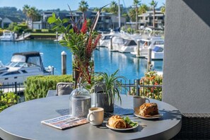 A round table with a newspaper, a glass jar, a mug, a plate with food, and a potted plant. - Villa One on the Waterways (Whitianga)
