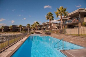 A swimming pool with a clear blue water, surrounded by palm trees and modern buildings. - Villa One on the Waterways (Whitianga)