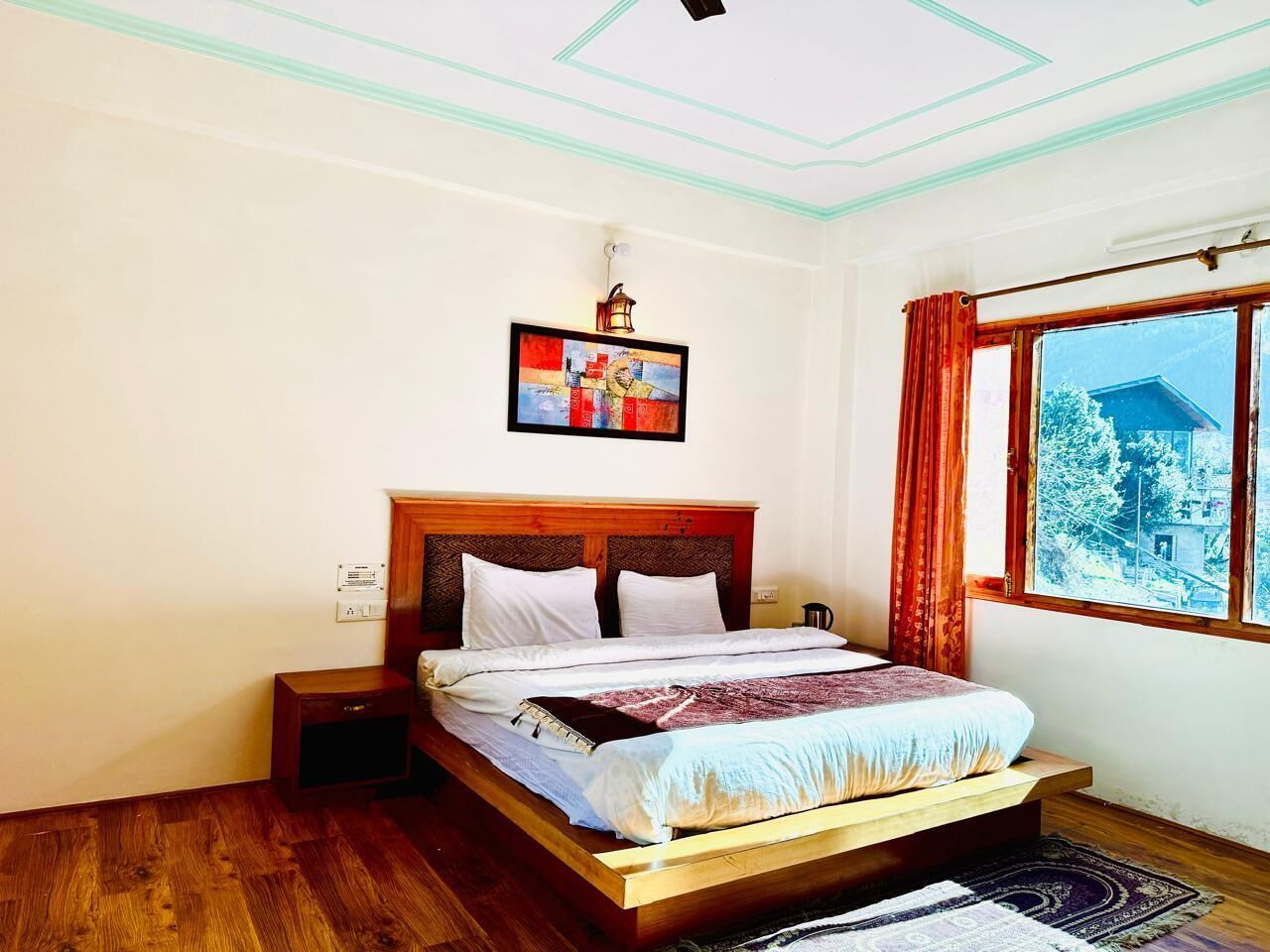 A bedroom with a wooden bed, a nightstand, a wall-mounted lamp, and a window with curtains.