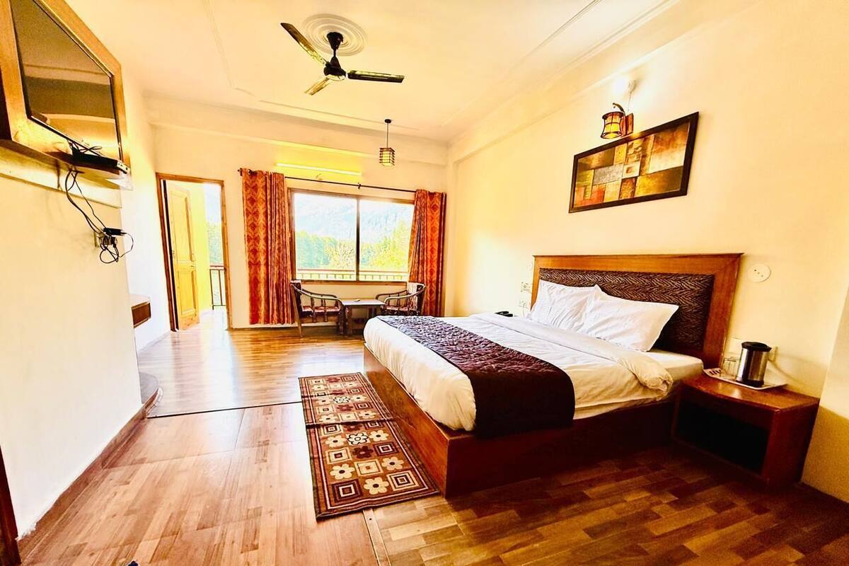 A bedroom with a bed, a nightstand, a ceiling fan, a window with curtains, and a door leading to another room.