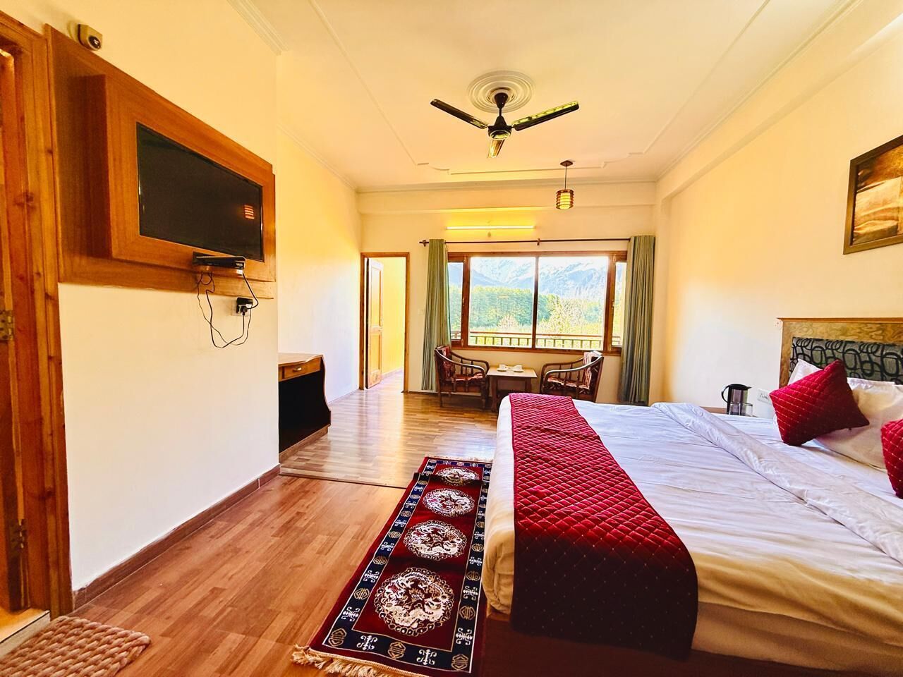 Un dormitorio con cama, ventilador de techo, televisor montado en la pared y vistas al exterior.