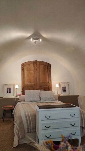 A bedroom with a wooden wardrobe, a bed with a striped bedspread, a white dresser with drawers, and two bedside tables with lamps.