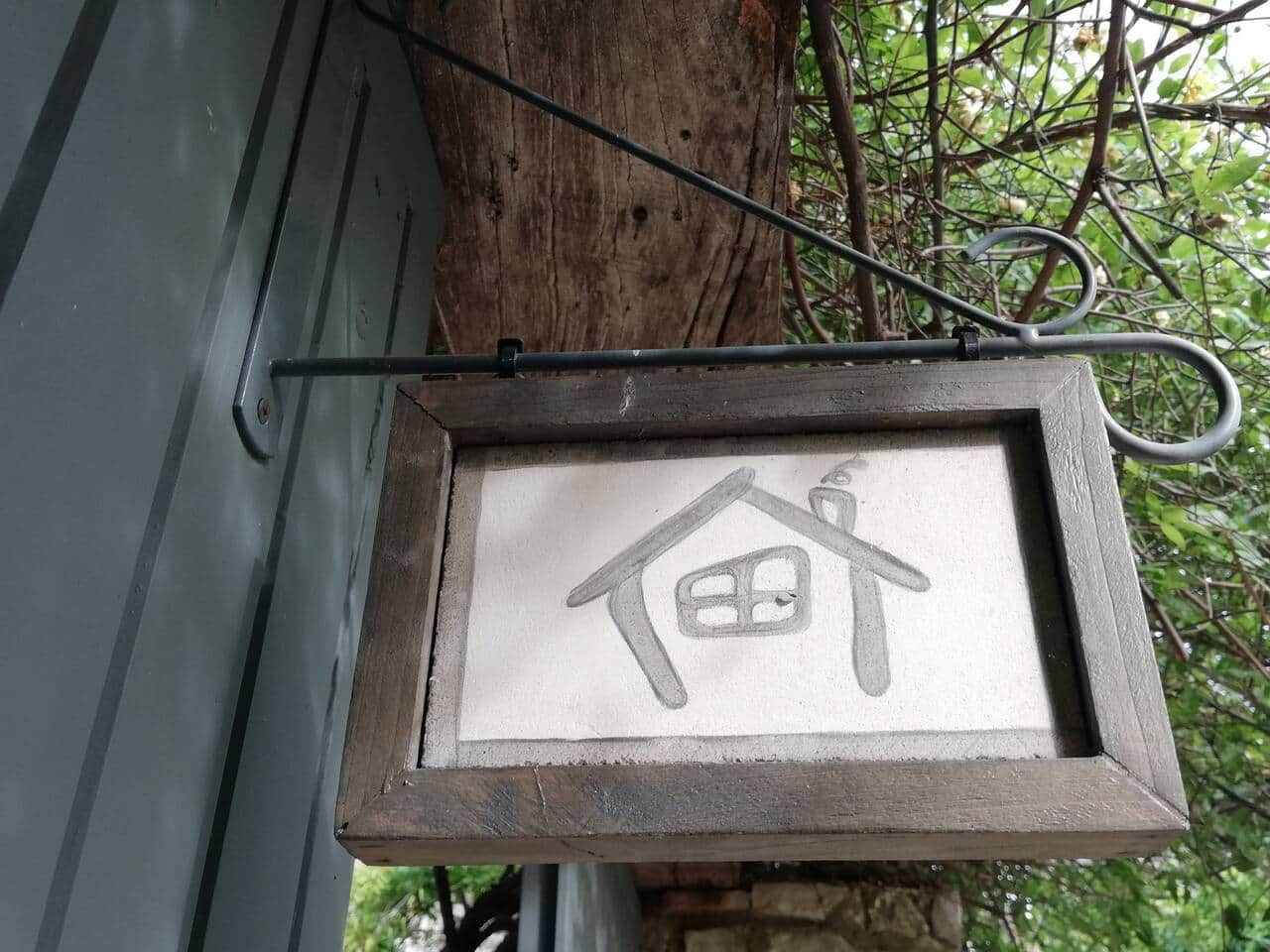 Une plaque de maison encadrée, suspendue à un support métallique.