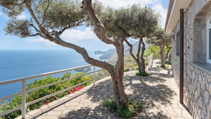 Un sentier en pierre bordé d’une rambarde, avec des arbres et une vue sur la mer.