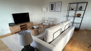 Een moderne woonkamer met een bank, salontafel, televisie, lamp en decoratieve elementen.