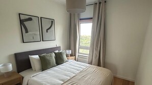 Een slaapkamer met een bed, twee nachtkastjes, een raam met gordijnen, en twee gekaderde abstracte kunstwerken aan de muur.