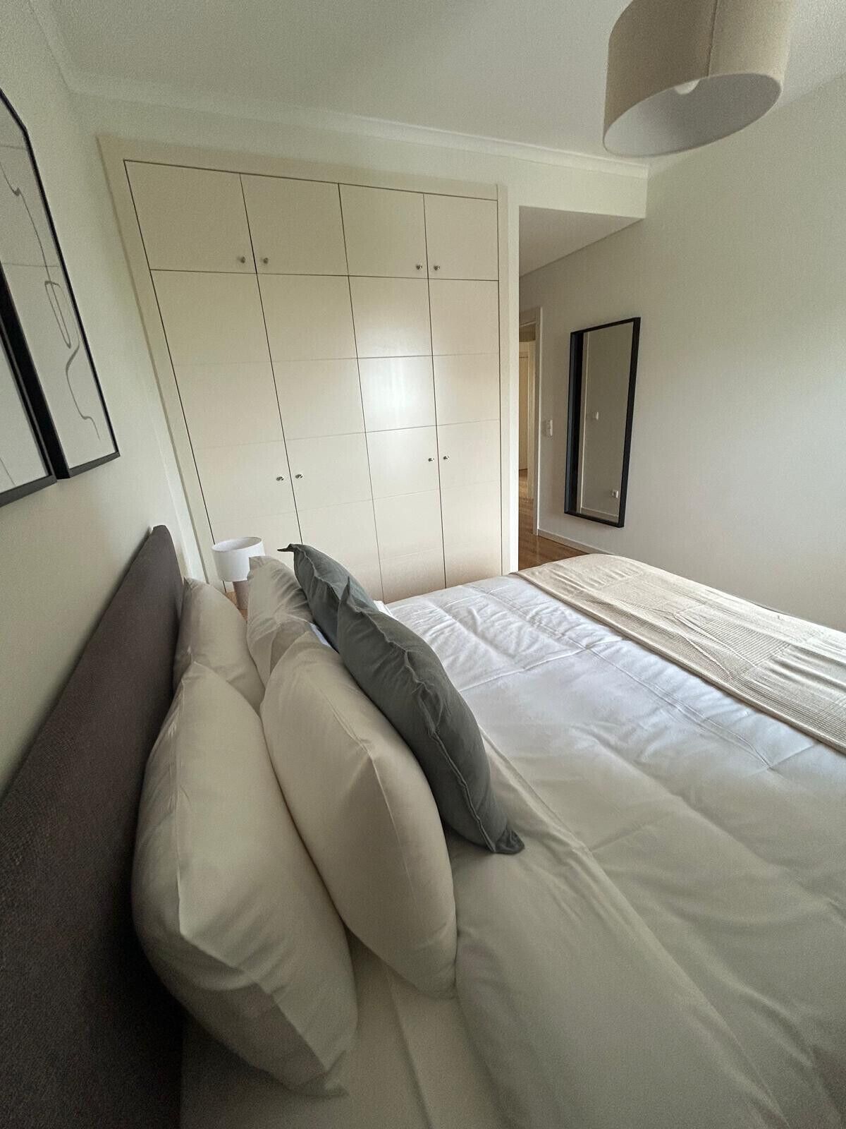 A bedroom with a bed, pillows, a wardrobe, and a mirror.