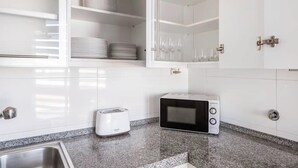 Een keuken met witte kastjes, een broodrooster, een magnetron en een spoelbak.