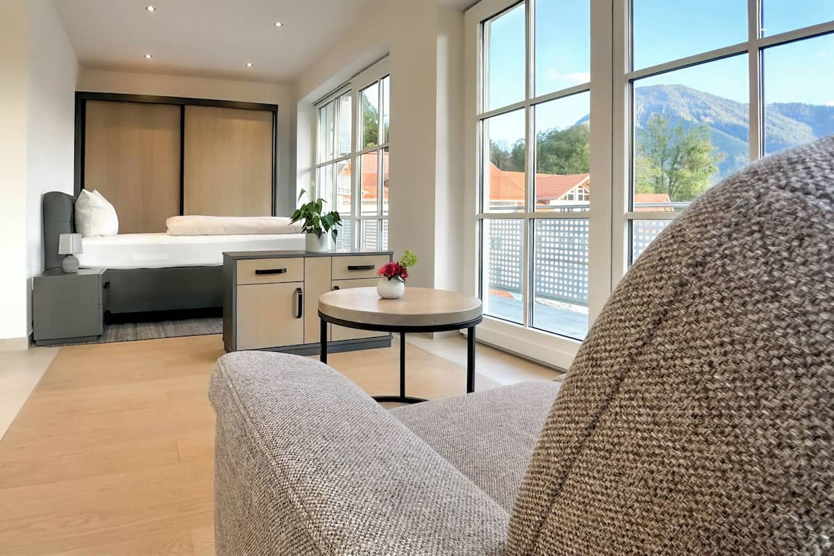 Une chambre d’hôtel moderne, dotée d’un lit, d’une table de chevet et offrant une vue sur les montagnes grâce à de grandes fenêtres.