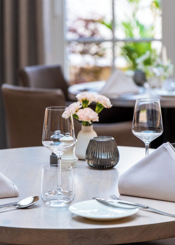 A dining table set with wine glasses, a vase with flowers, and a candle.