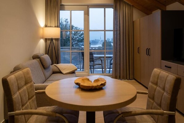 A cozy living area with a sofa, a round table with a wooden bowl, and a TV on the wall.