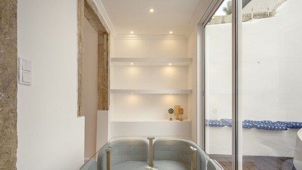 Un interior moderno con una mesa de vidrio, sillas tapizadas en gris y una pared blanca con estanterías.