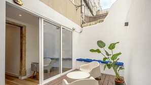 Un balcón con mesa y sillas, una planta en maceta y un ventanal corredero que da a un espacio interior.