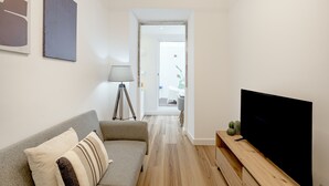 Una sala moderna con un sofá, un televisor de pantalla plana, una lámpara y un pequeño cactus sobre una mesa de madera.