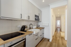 Een moderne keuken met een ingebouwde oven, magnetron en spoelbak, houten aanrechtbladen en een gang naar andere kamers.