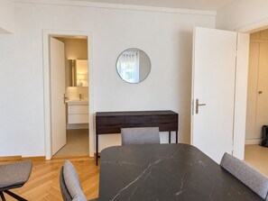 Ein Zimmer mit Esstisch, Stühlen, Schreibtisch, Spiegel und einer Tür zu einem Badezimmer.