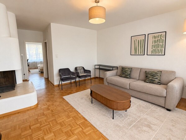 A living room with a sofa, two armchairs, a coffee table, a fireplace, and a ceiling light fixture. - Stylish 2-Bedroom Apartment with Stunning Views of Zurich - Tilia 41 (Zürich)