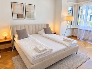 A double bed with a headboard, bedside tables with lamps, a window with sheer curtains, and a floor lamp. - Stylish 2-Bedroom Apartment with Stunning Views of Zurich - Tilia 41 (Zürich)