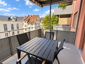 Ein Balkon mit Tisch und Stühlen und Blick auf Gebäude, umzäunt mit einem Maschendrahtzaun.