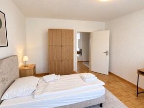 Une chambre à coucher comprenant un lit, une lampe de chevet, une armoire et une porte donnant sur une autre pièce.