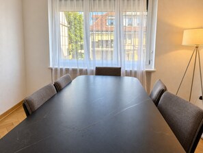A conference room with a long table, four chairs, a window with sheer curtains, and a floor lamp. - Stylish 2-Bedroom Apartment with Stunning Views of Zurich - Tilia 41 (Zürich)