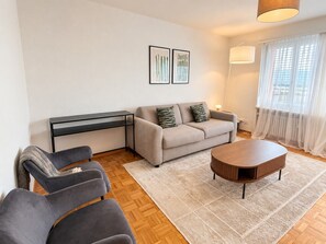 Ein Wohnzimmer mit einer Couch, Sesseln, einem Couchtisch, einem Beistelltisch und einer Lampe.