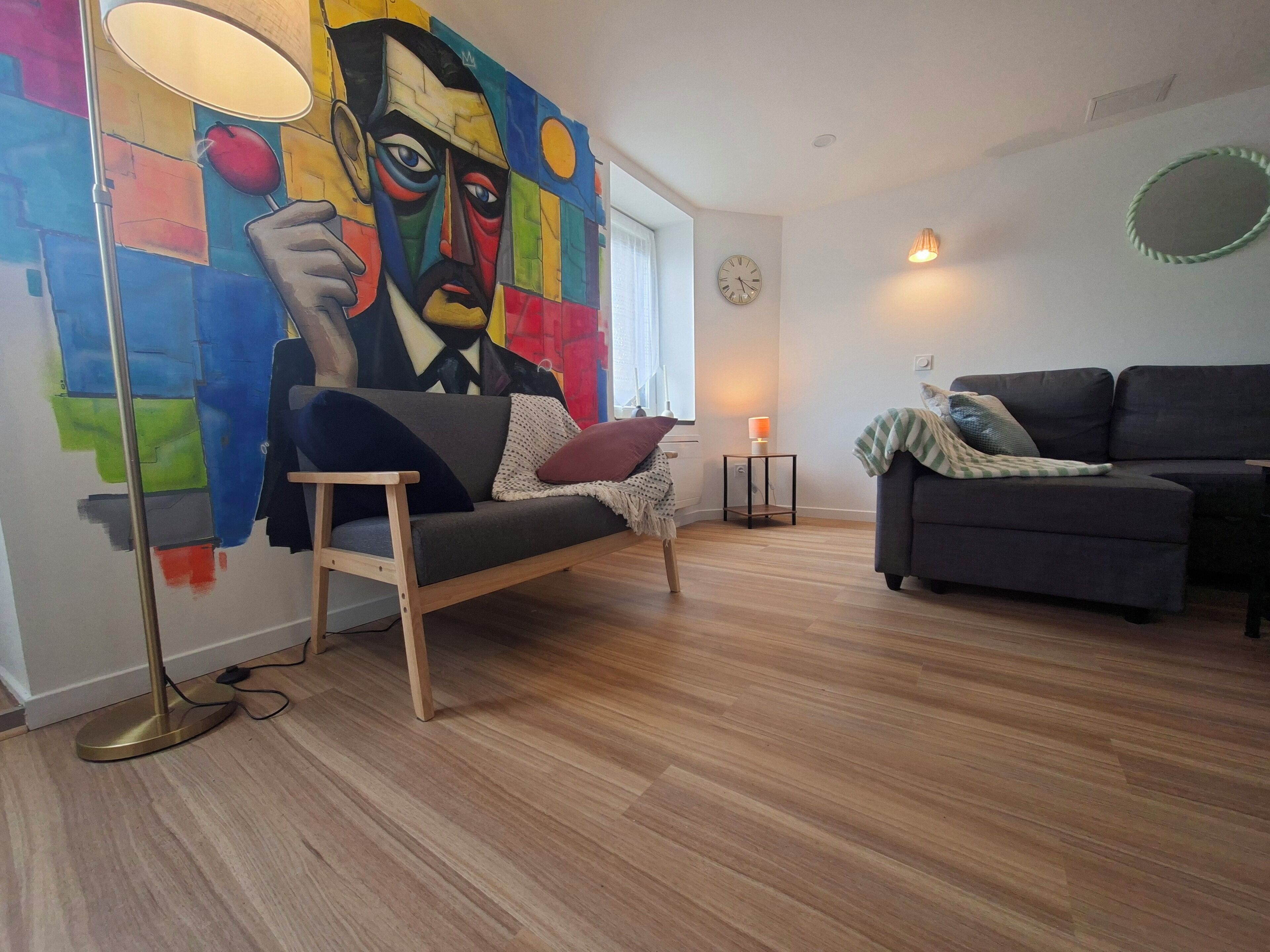 Ein Wohnzimmer mit einem modernen Sofa, einer Stehlampe, einem kleinen Tisch mit Lampe und einem farbenfrohen, abstrakten Gemälde an der Wand.