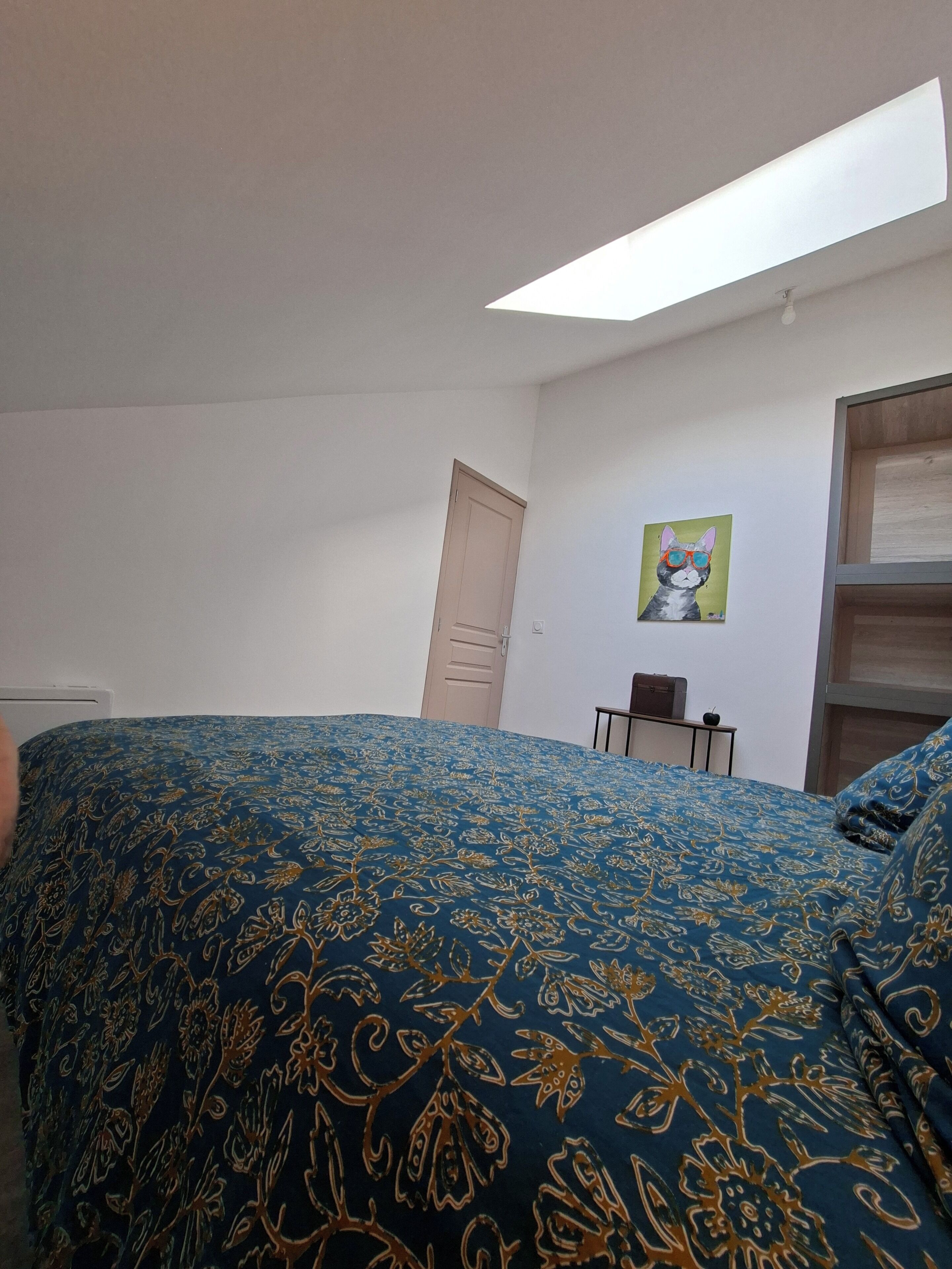 A bedroom with a bed, a door, a small table, and a painting on the wall.