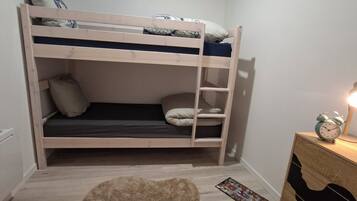 A bunk bed with a wooden frame, a small rug, a dresser, and a clock on the dresser.