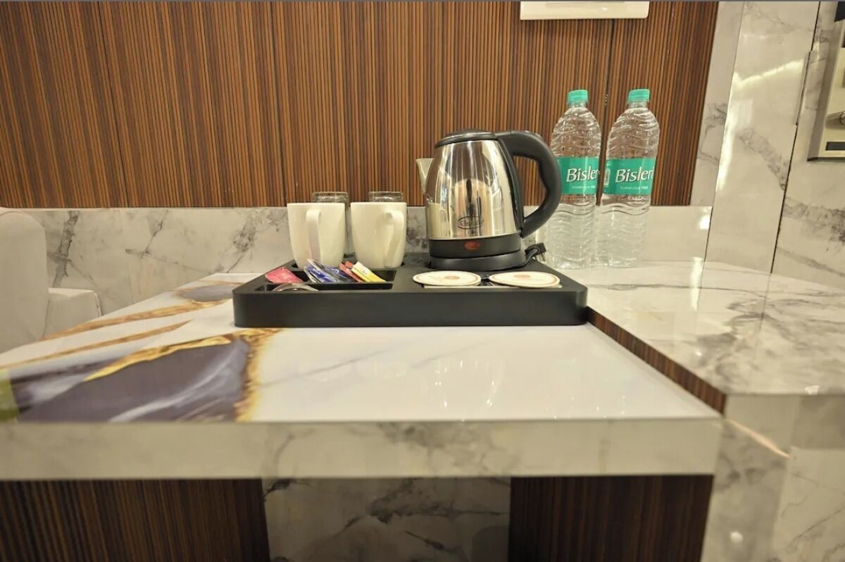 A hotel room with a marble countertop, a coffee maker, two Bisleri water bottles, and three white mugs.