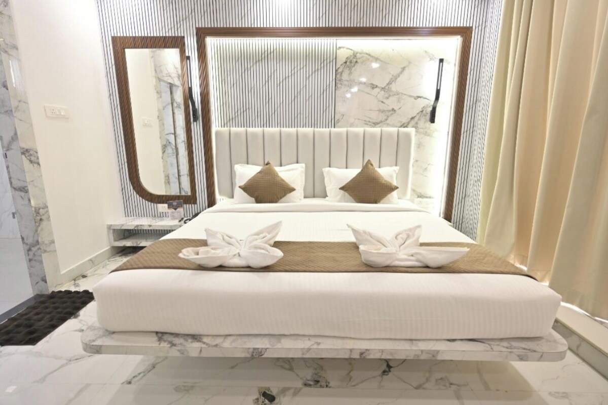 Habitación de hotel con cama, un espejo grande, cabecera de mármol y ventana con cortinas.