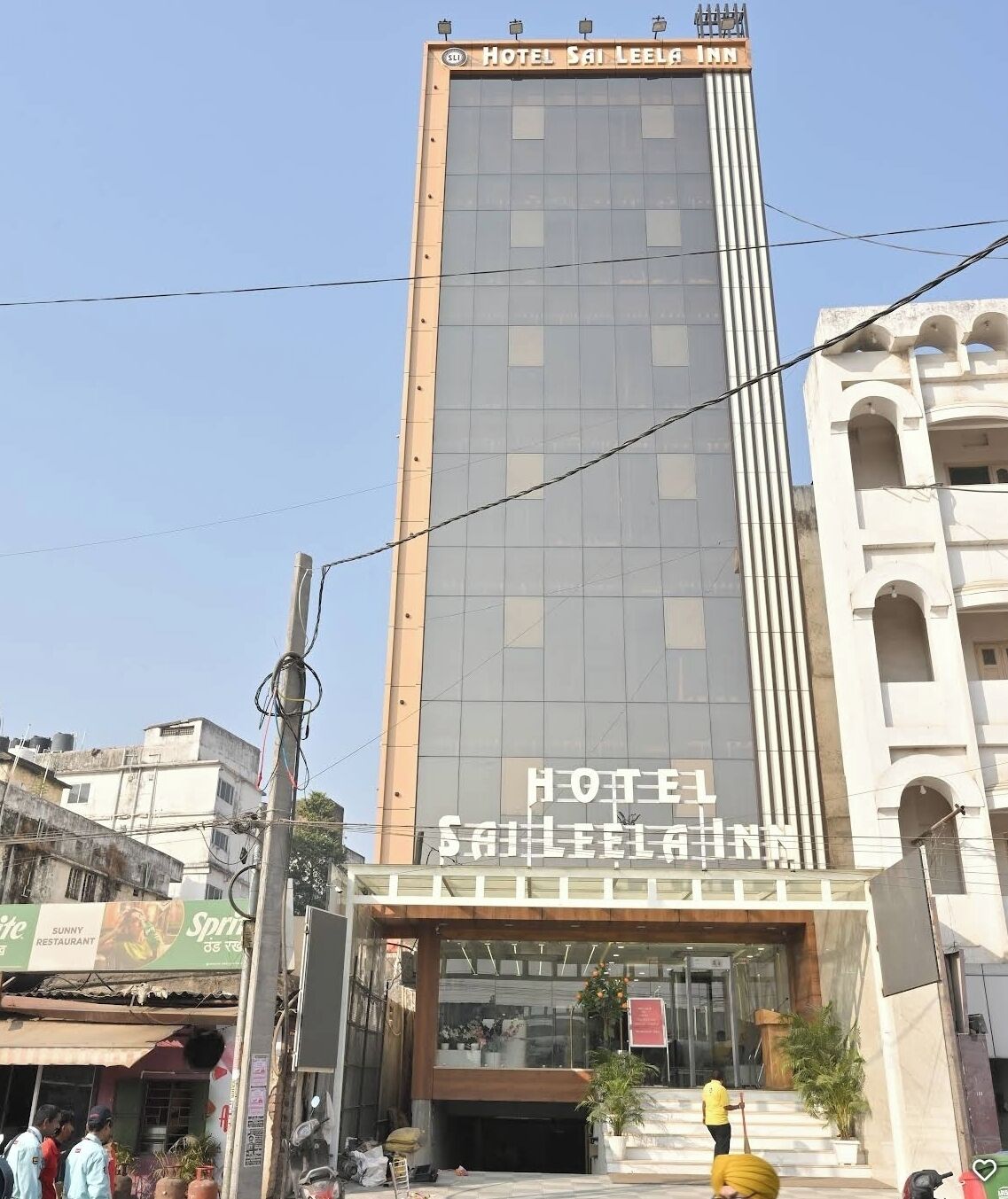 Un edificio de hotel alto con fachada moderna de vidrio y un letrero que dice 'HOTEL SAI LEELA INN'.